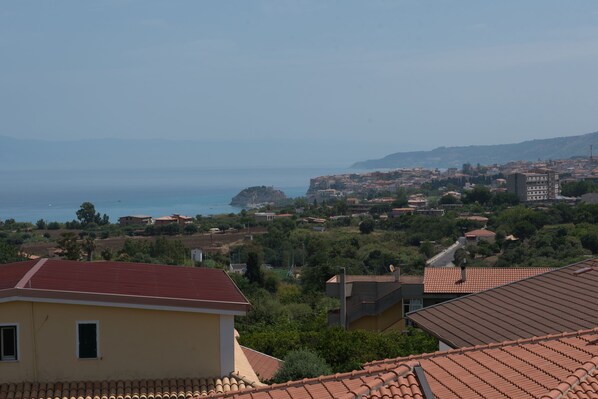 Uma vila costeira com edifícios de telhados em terracota, um afloramento rochoso proeminente e vista para o mar.