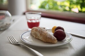 Un plato con un pastel, dos frutas y un vaso de bebida roja sobre una mesa.