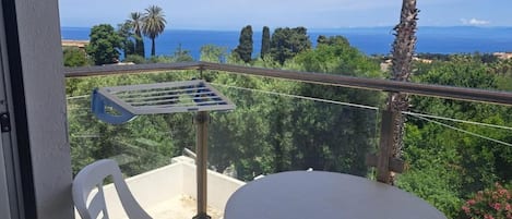 Un balcón con vista al mar, una silla blanca y una mesa redonda.