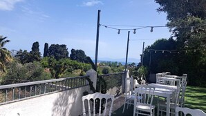 Un patio al aire libre con mobiliario blanco, vistas del paisaje y luces colgantes.