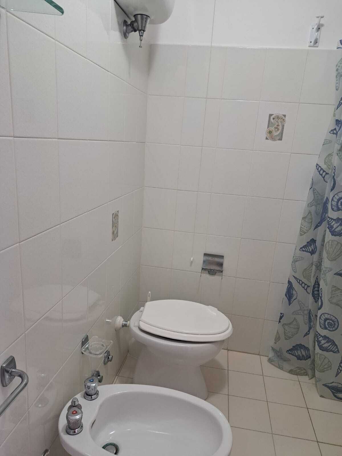 Une petite salle de bain comprenant des toilettes, un bidet et un rideau de douche orné d’un motif de coquillages.