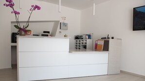 Una recepción con un mostrador blanco, un jarrón con flores moradas y un cuadro en la pared.