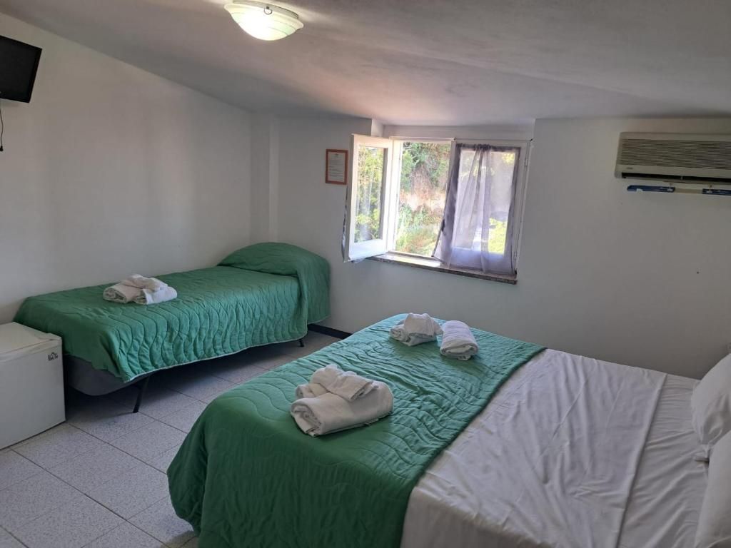 A room with two beds, a window with curtains, an air conditioning unit, and a television on the wall.