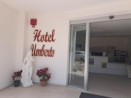 A hotel entrance with a reception desk, a statue, and potted plants.