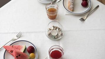 Une table avec une assiette de pastèque, des raisins et un verre de boisson rouge ; une autre assiette avec une pâtisserie et des fruits ; un verre de jus d’orange ; et un petit plat contenant des noix et des graines.