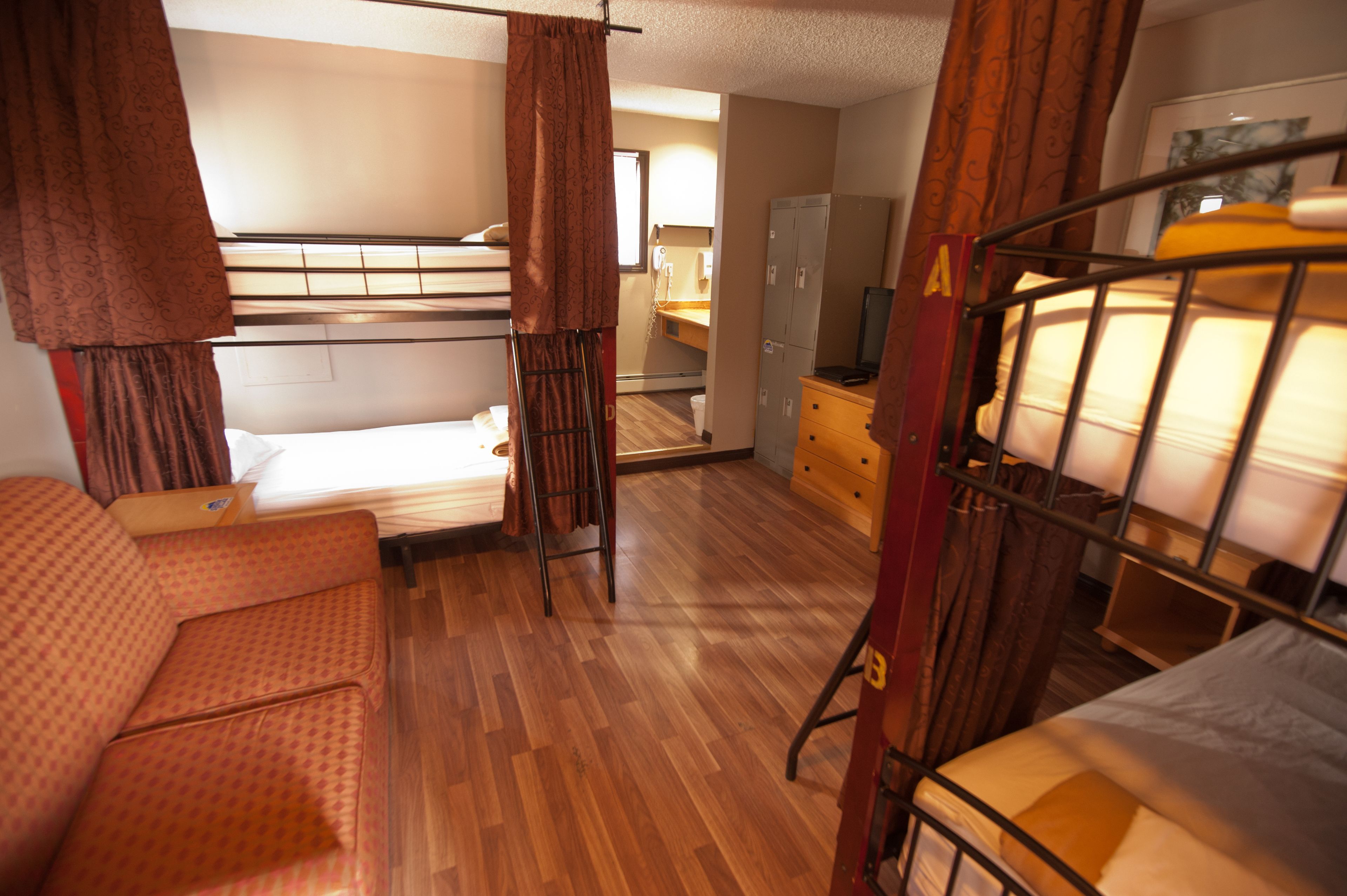 A dormitory room with bunk beds, a sofa, a desk, and a wardrobe.
