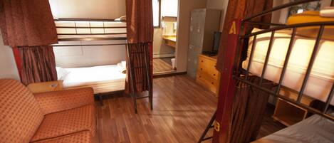 A dormitory room with bunk beds, a sofa, a desk, and a wardrobe.