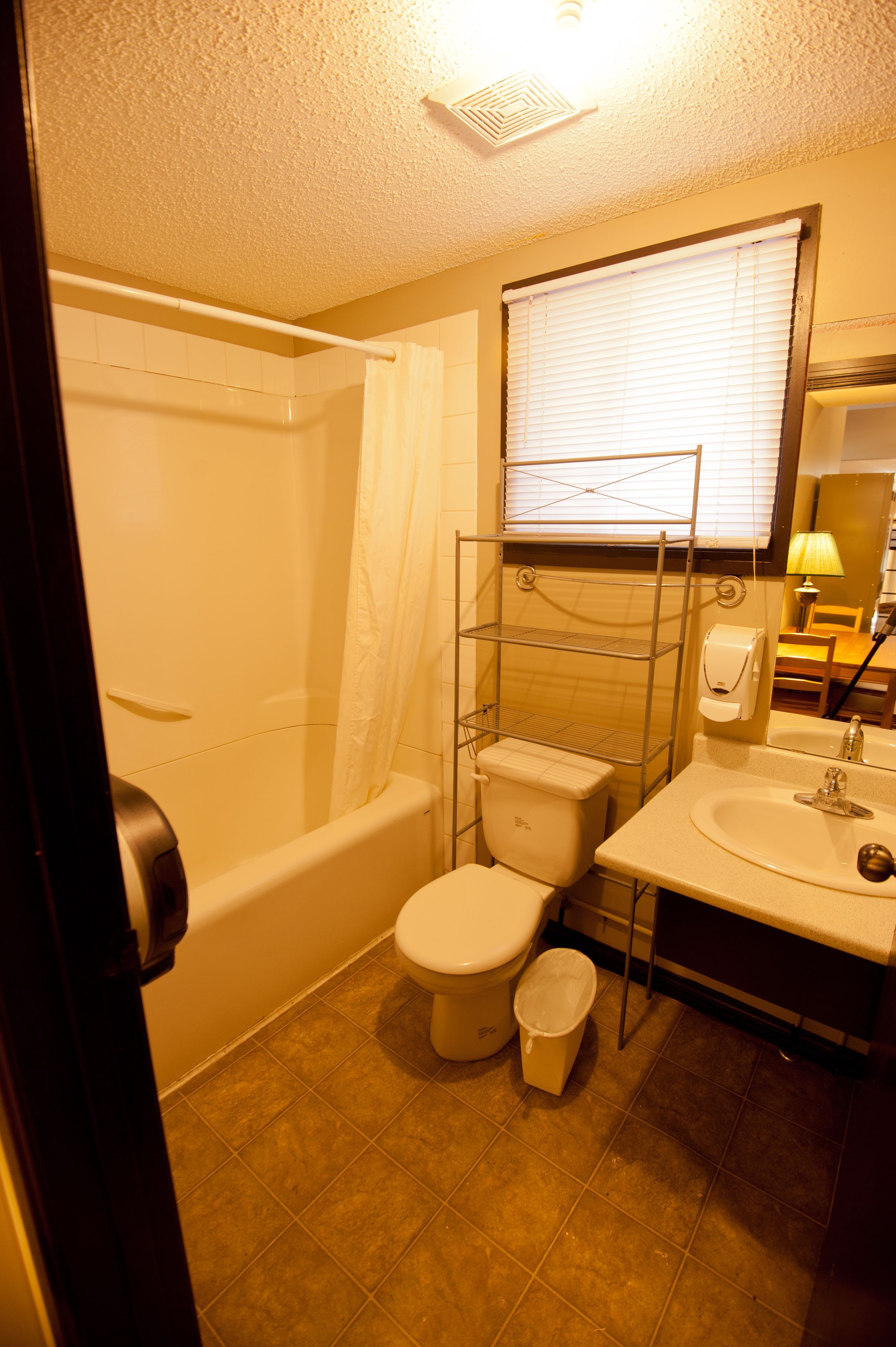 A bathroom with a bathtub, toilet, sink, and a shelf with toiletries.
