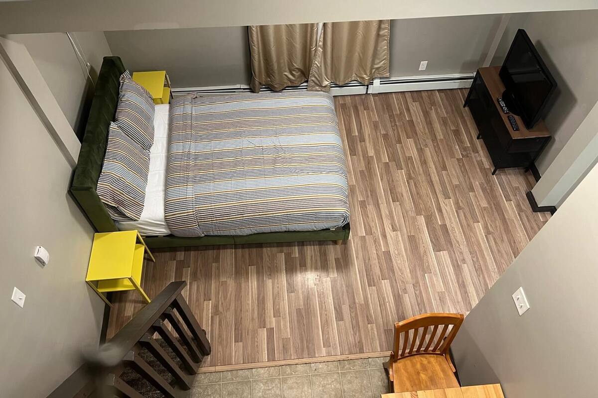 A small, compact room with a bed, a wooden table, a chair, and a small desk with a computer.