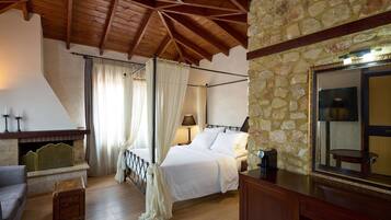 A bedroom with a stone wall, wooden ceiling beams, a bed with white linens, a nightstand with a lamp, and a wooden chest of drawers.