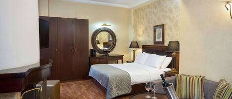 Une chambre d’hôtel avec un lit, un canapé, une table ronde, une télévision, un miroir et une cheminée.