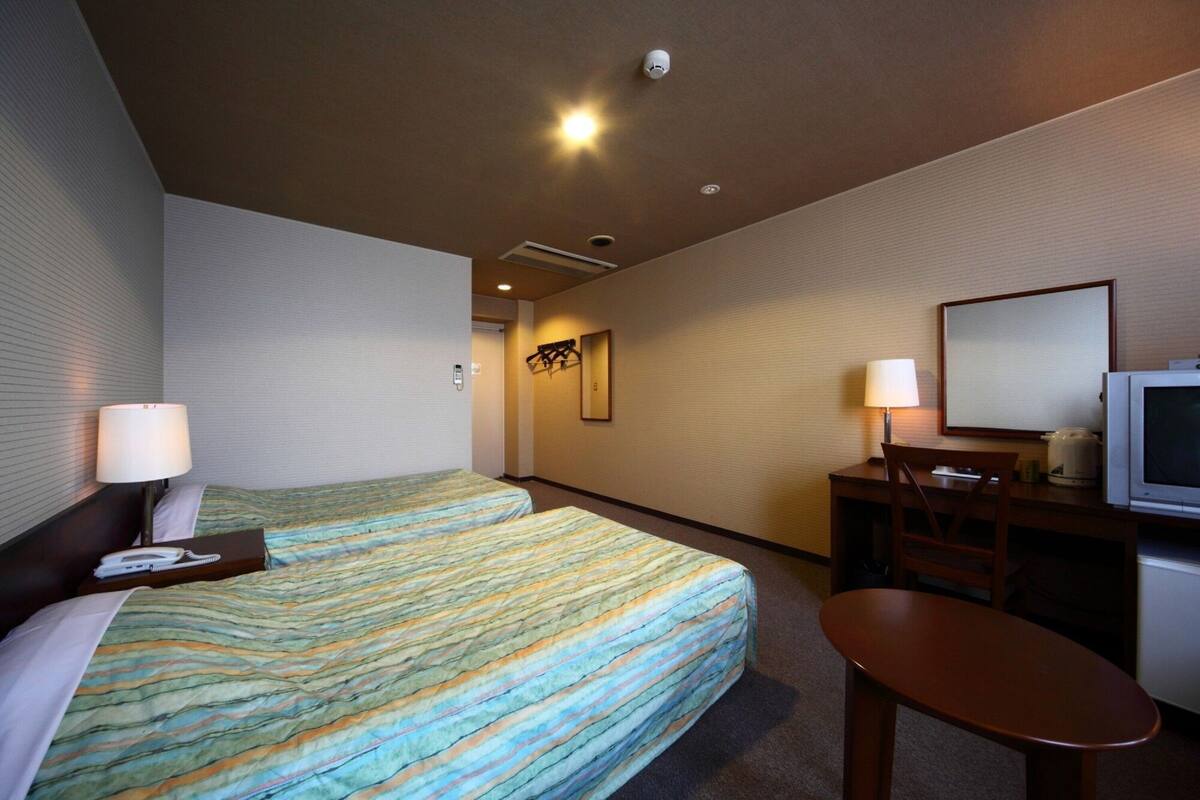 A hotel room with two beds, a desk with a chair, a television, and a mirror.