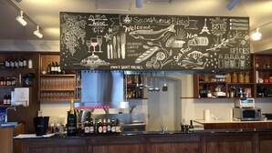 A bar area with a chalkboard menu, shelves of bottles, and a kitchen in the background. - Hotel Asyl Nara Annex (Nara)