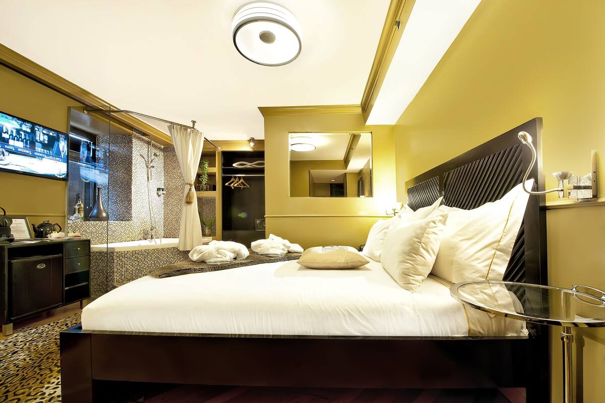 Een hotelkamer met een groot bed, een televisie aan de muur, een spiegel en een douche.