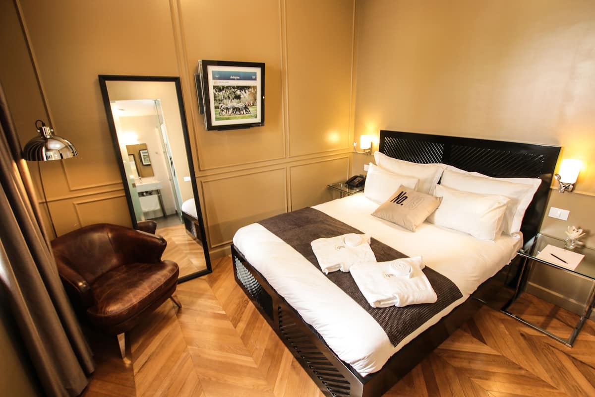 Een hotelkamer met een bed, een stoel, een nachtkastje, een spiegel en een lijst aan de muur.
