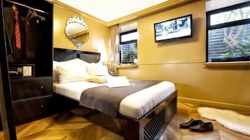A hotel room with a bed, a wardrobe, a mirror, a television, and a window with a plant.