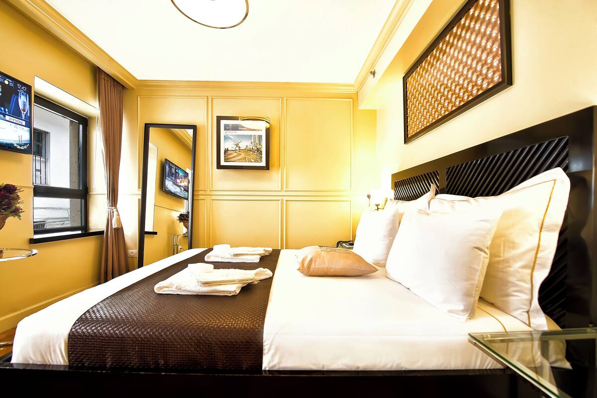 Een hotelkamer met een keurig opgemaakt bed, een grote spiegel en een foto in een lijst aan de muur.