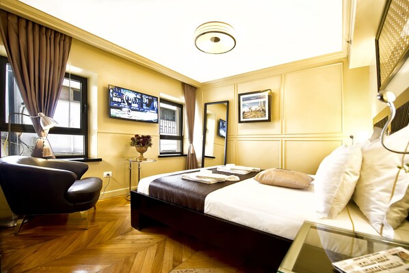 Une chambre d’hôtel avec un lit, une chaise, un bureau avec un ordinateur portable, une télévision et une fenêtre avec des rideaux.