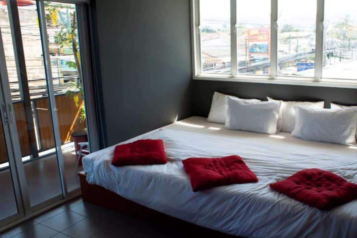 A hotel room with a large bed, white bedding, and red pillows.