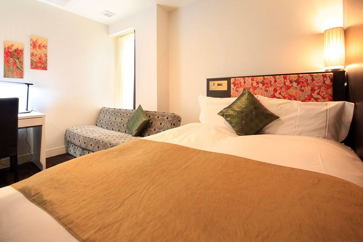 A hotel room with a large bed, a desk, a chair, and two wall-mounted lamps.