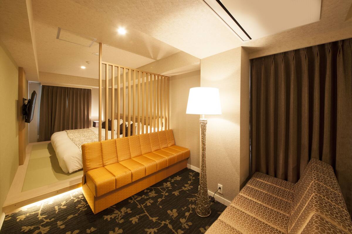 A hotel room with a bed, a sofa, a lamp, and a patterned carpet.