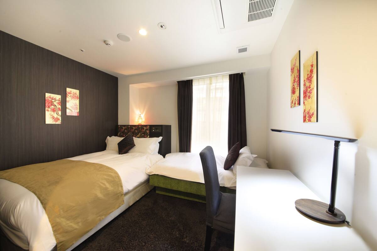 A hotel room with two beds, a desk, a chair, a desk lamp, and artwork on the walls.