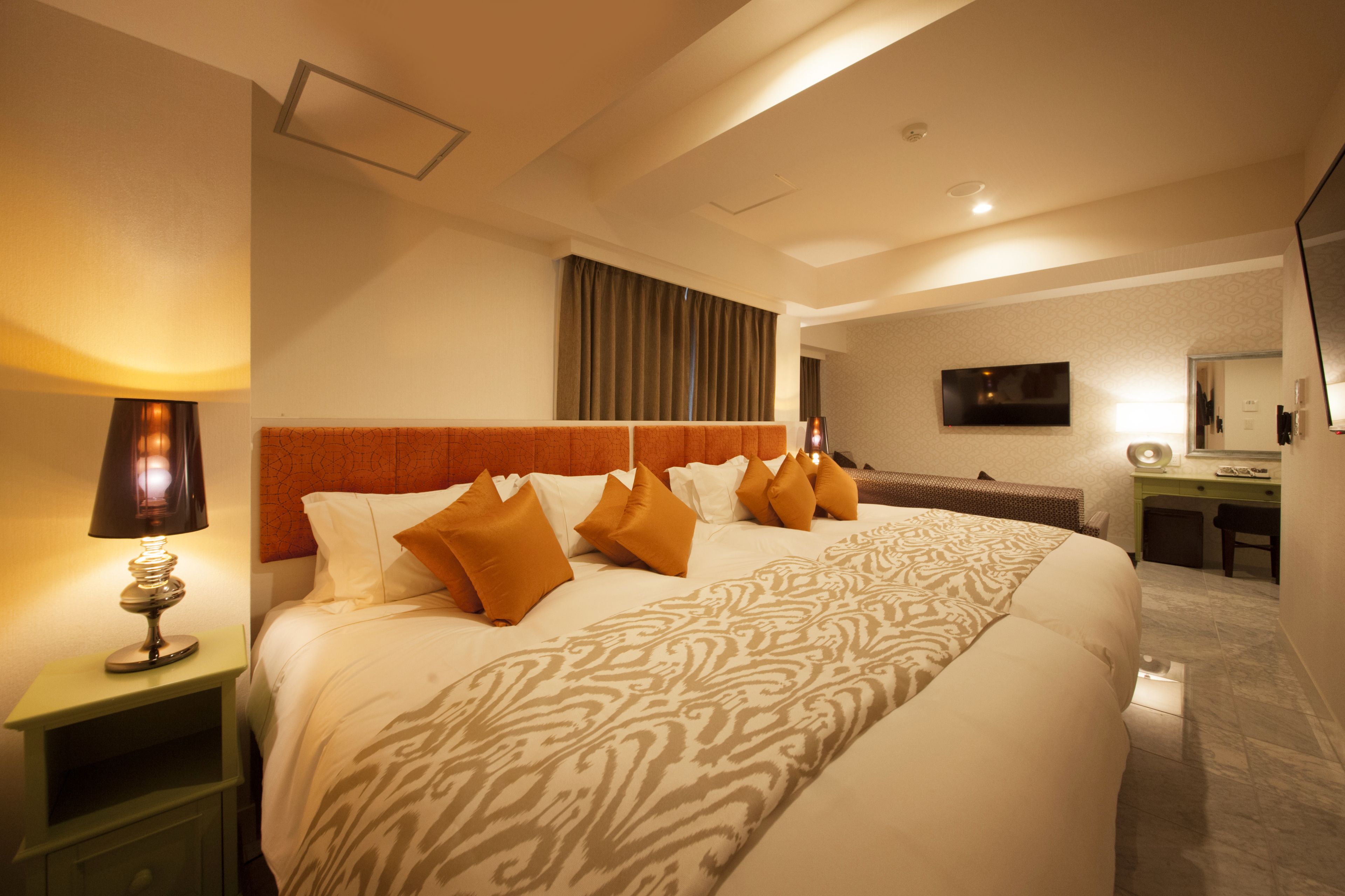 A hotel room with a large bed, a desk, a chair, a TV, and a lamp.