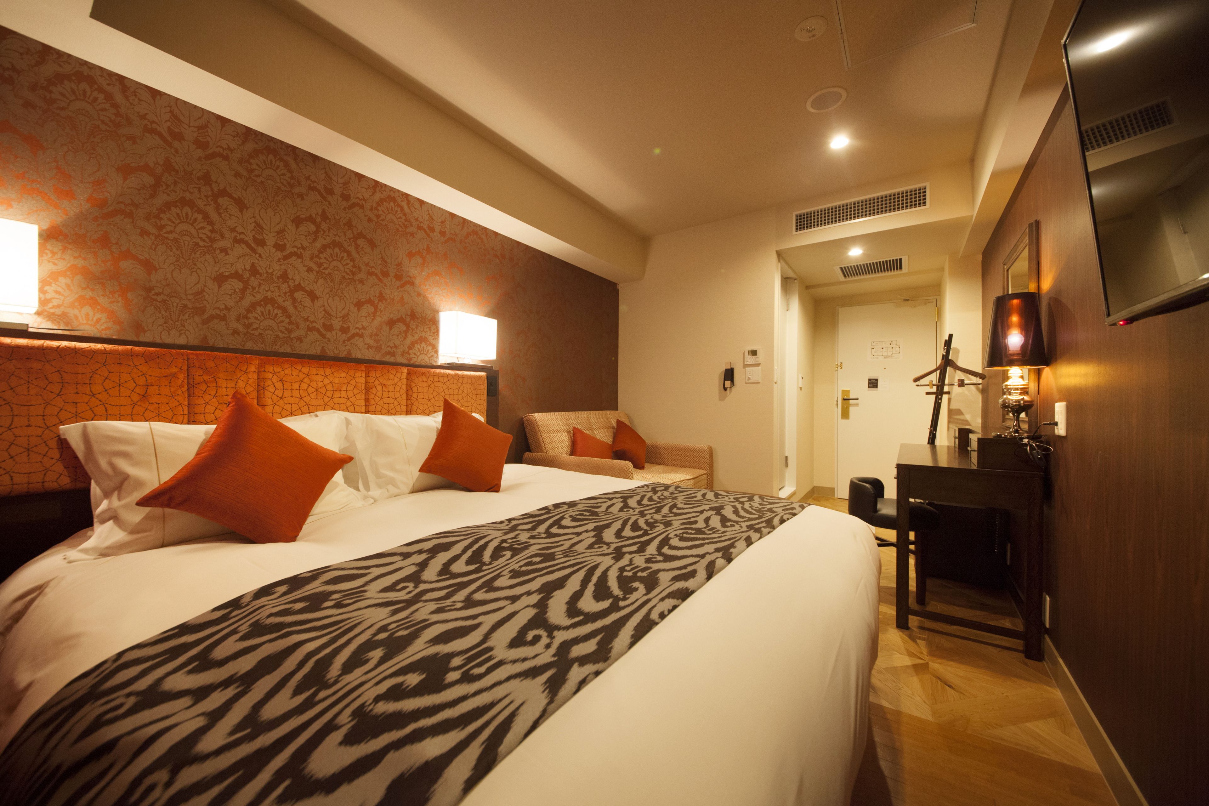 A hotel room with a large bed, two pillows, a patterned throw, a desk, and a TV.