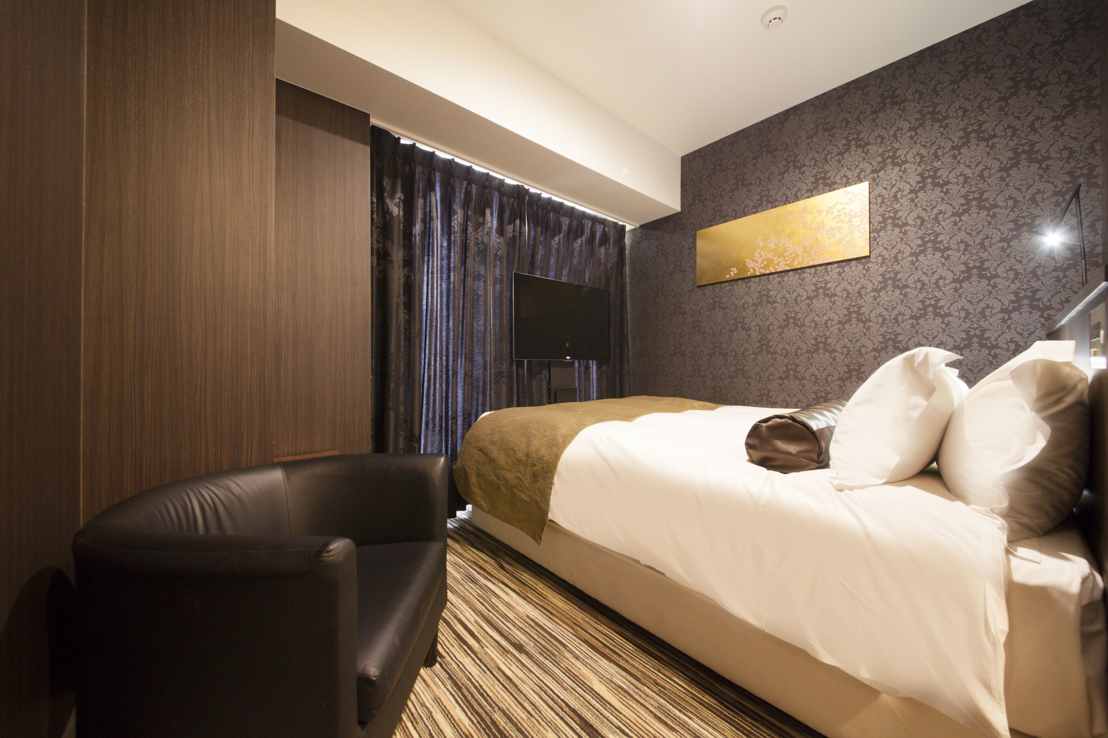 Une chambre d’hôtel avec un grand lit, un téléviseur à écran plat, un fauteuil en cuir et une moquette à motifs.