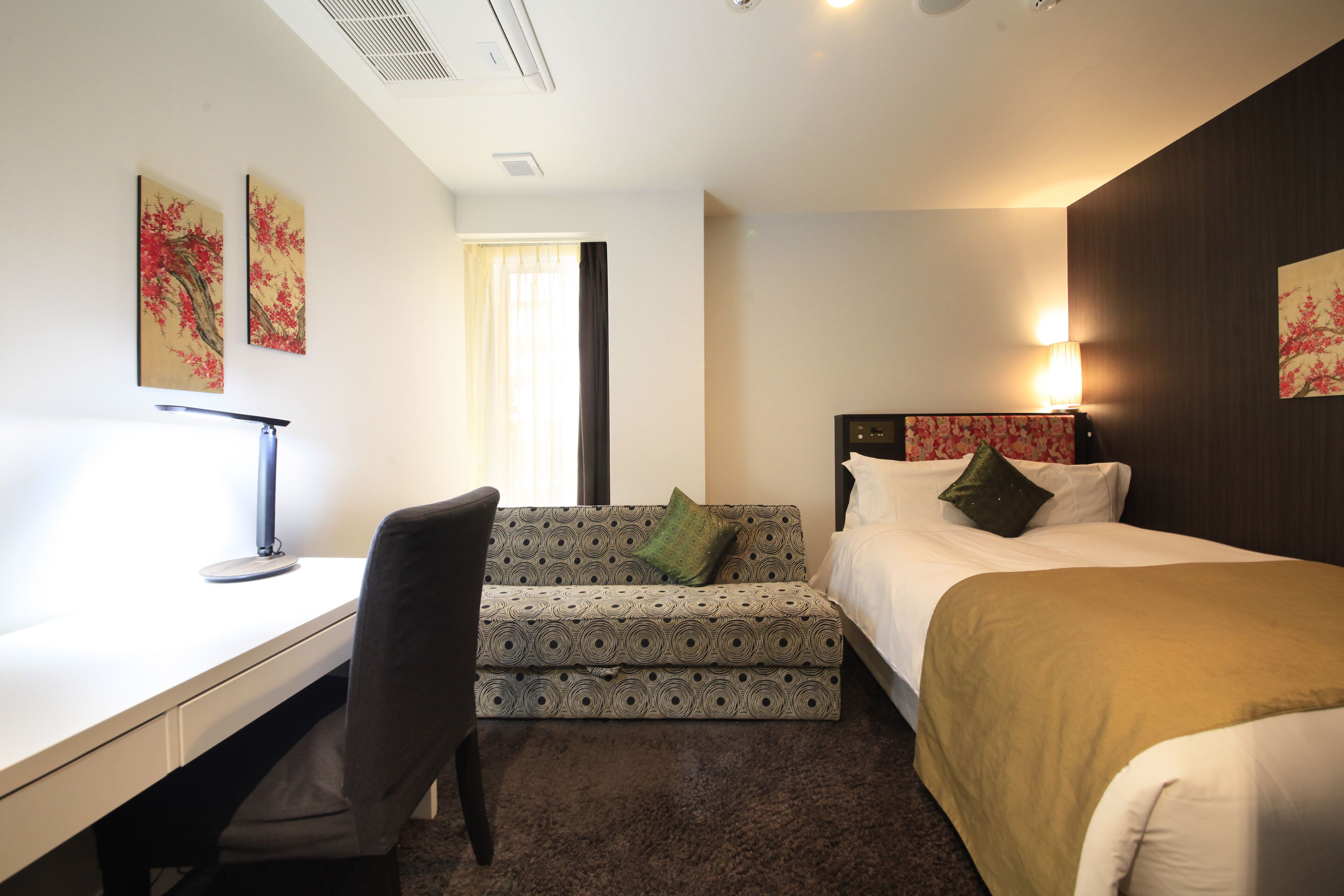 A hotel room with a desk, a sofa, a bed, and two paintings on the wall.