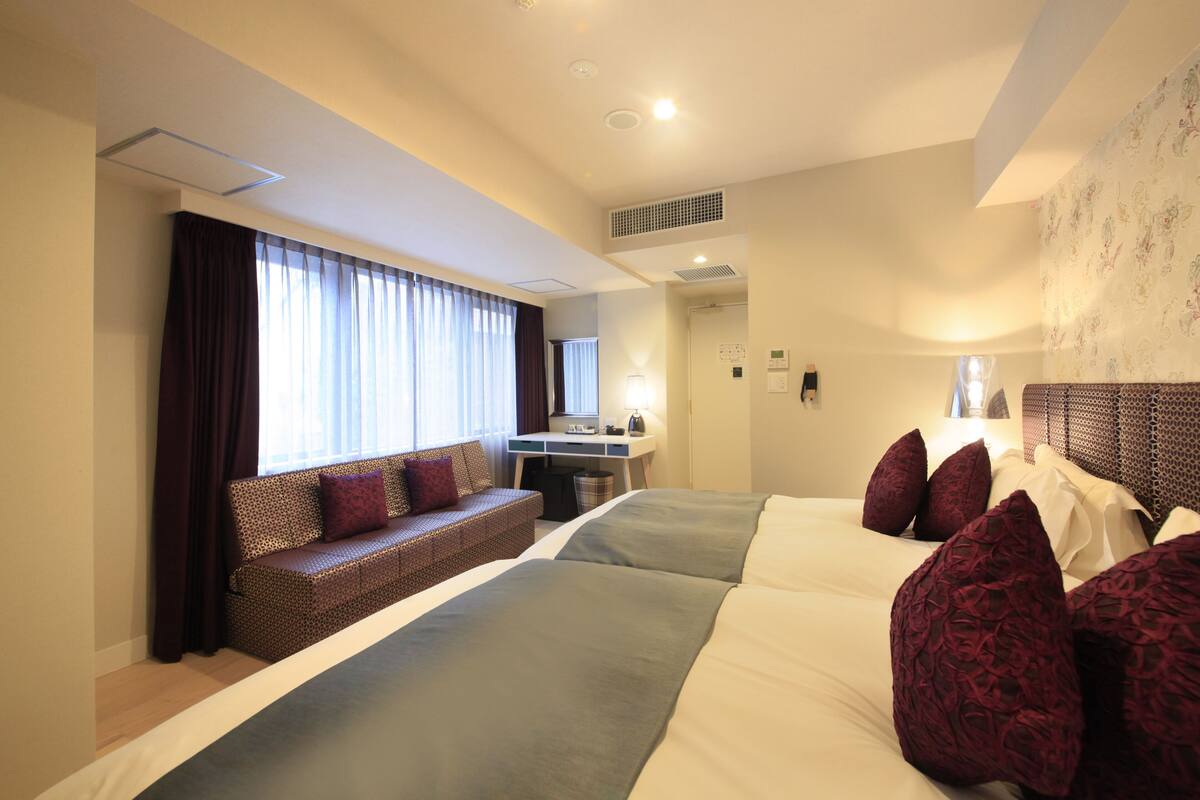A hotel room with a large bed, a sofa, a desk, and a window with curtains.