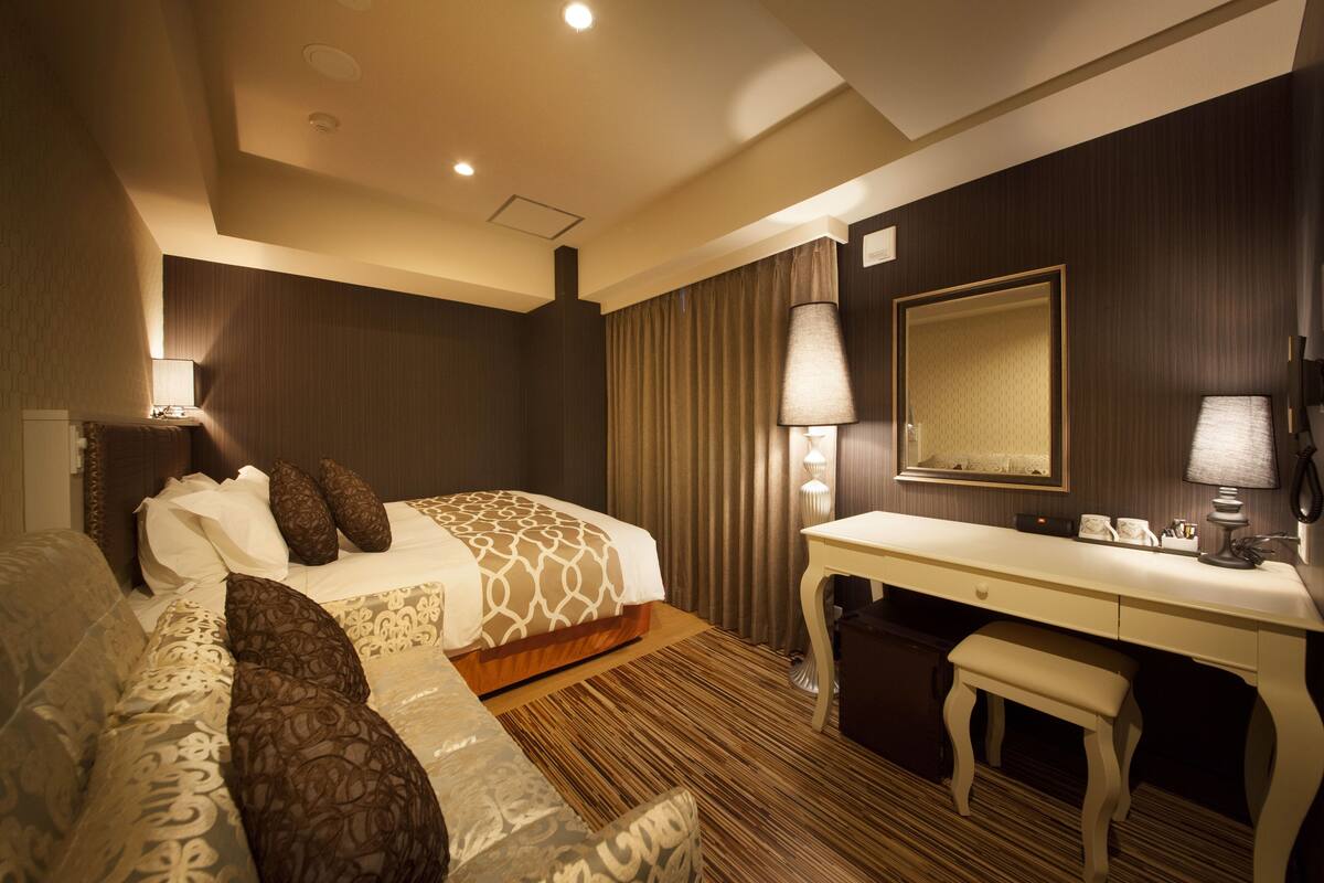 A hotel room with a bed, a desk, a chair, a lamp, and a mirror.