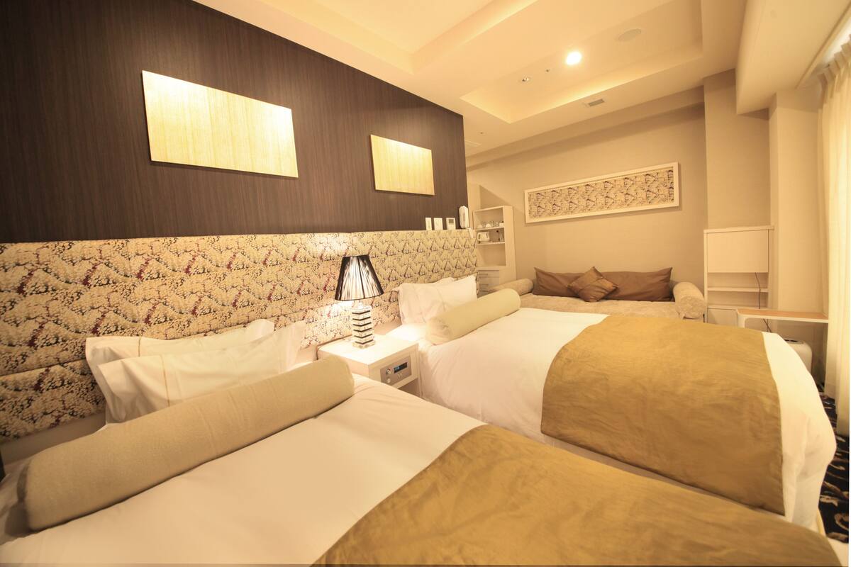 A hotel room with two beds, a patterned headboard, a bedside table with a lamp, and a wall-mounted artwork.