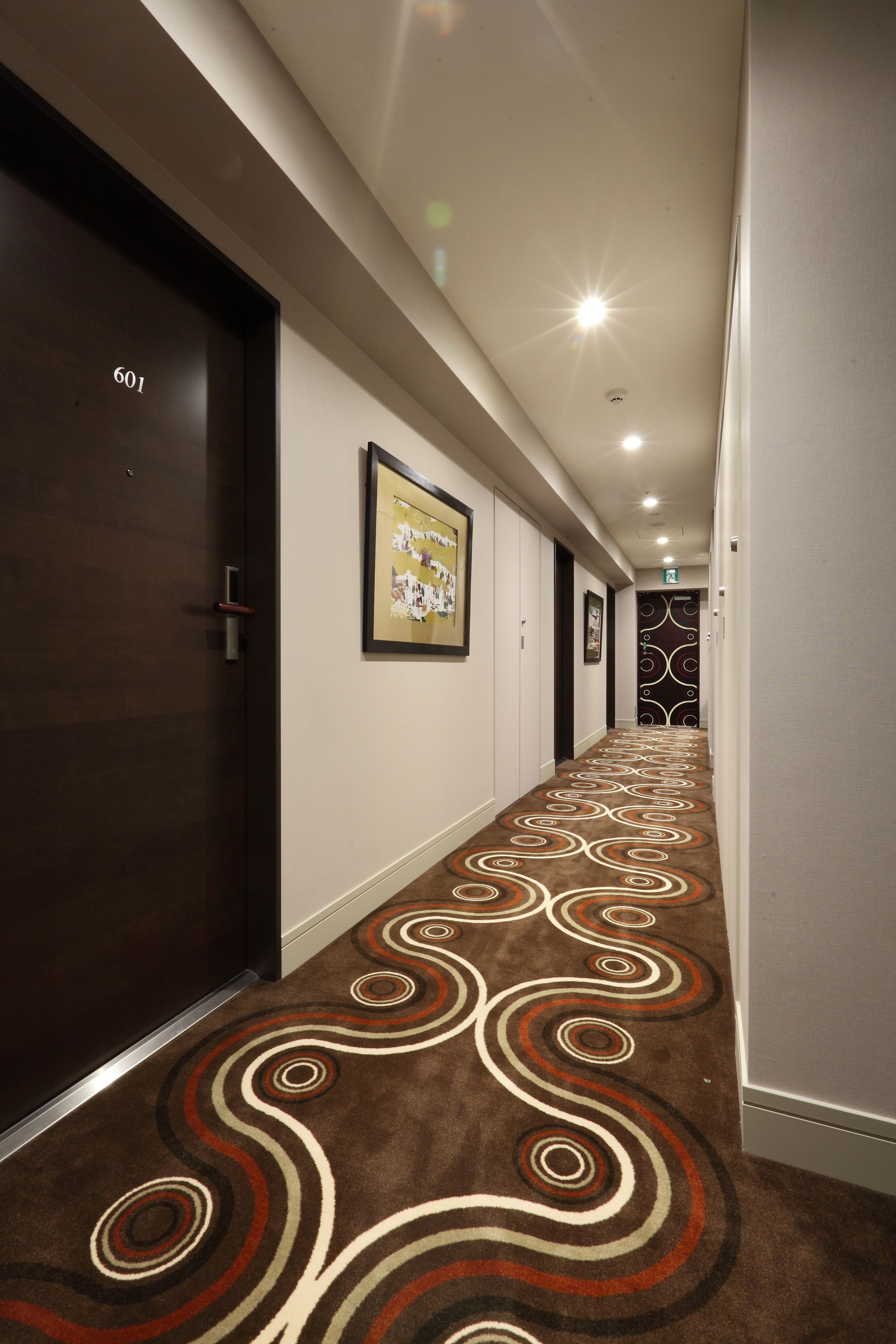 A hotel hallway with a patterned carpet, framed pictures on the walls, and a door labeled '601'.