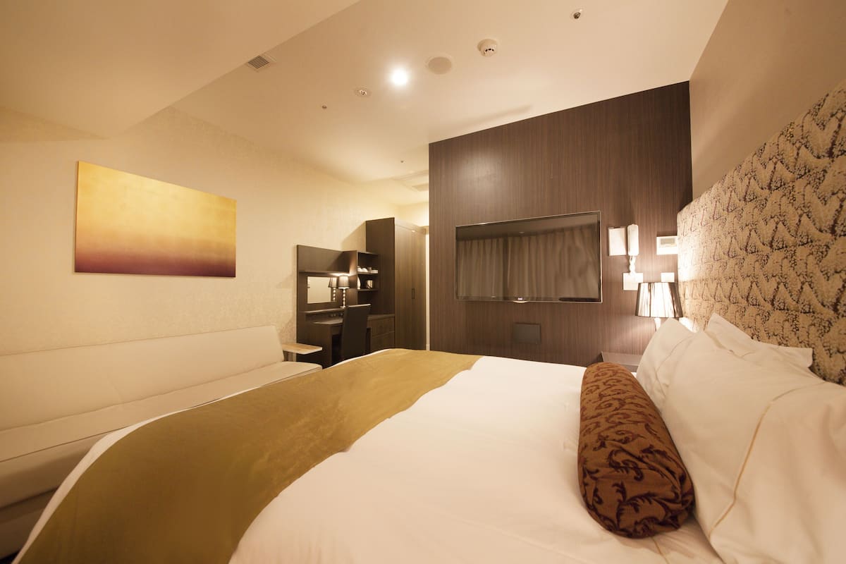 A hotel room with a bed, a desk, a chair, a TV, and a painting on the wall.