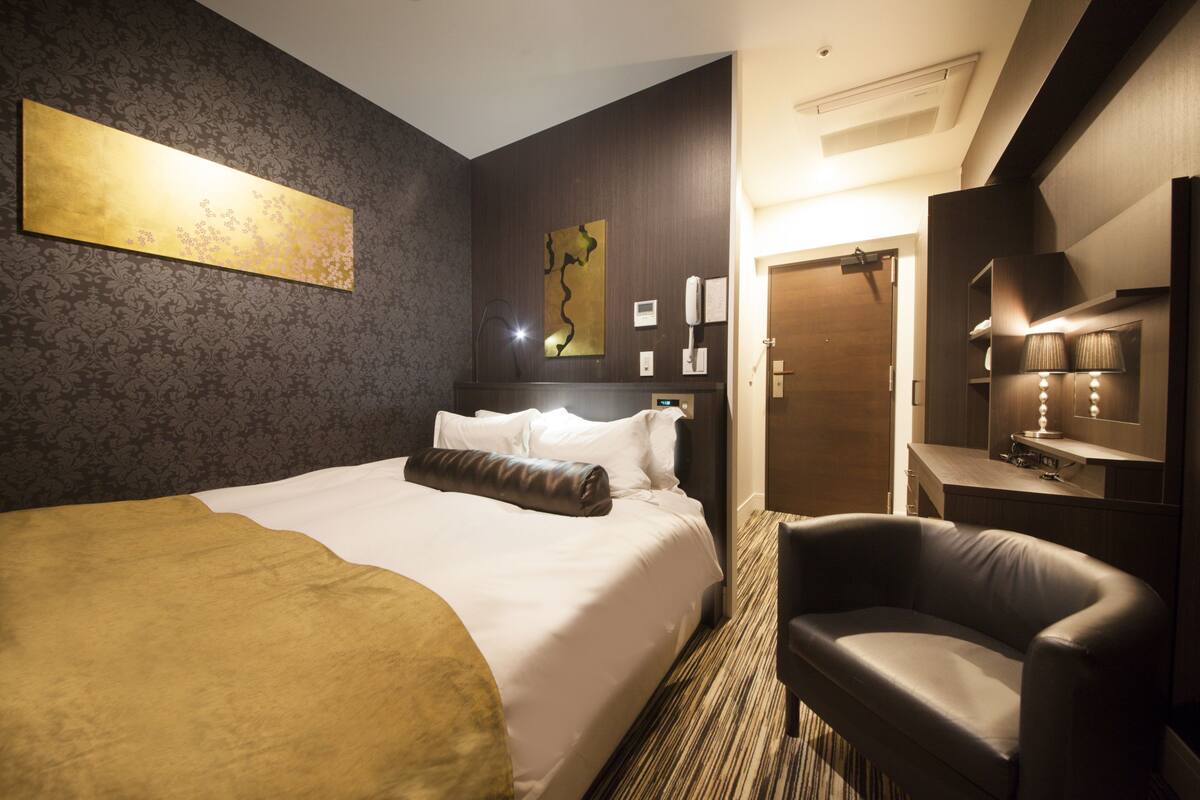 A hotel room with a large bed, a desk with a lamp, a chair, and a painting on the wall.