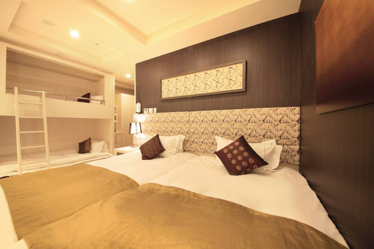 A hotel room with a bunk bed, a large bed with patterned headboard, and a wall-mounted artwork.