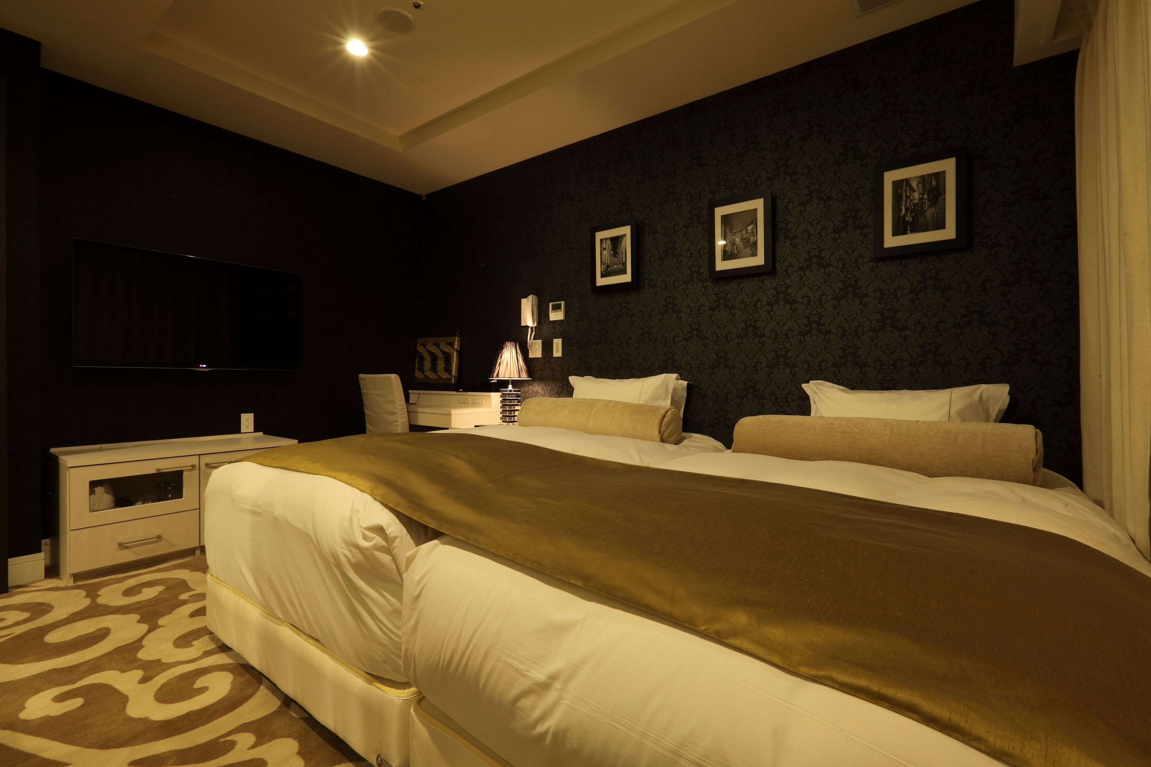A hotel room with a large bed, a flat-screen TV mounted on the wall, a bedside table with a lamp, and framed pictures on the wall.