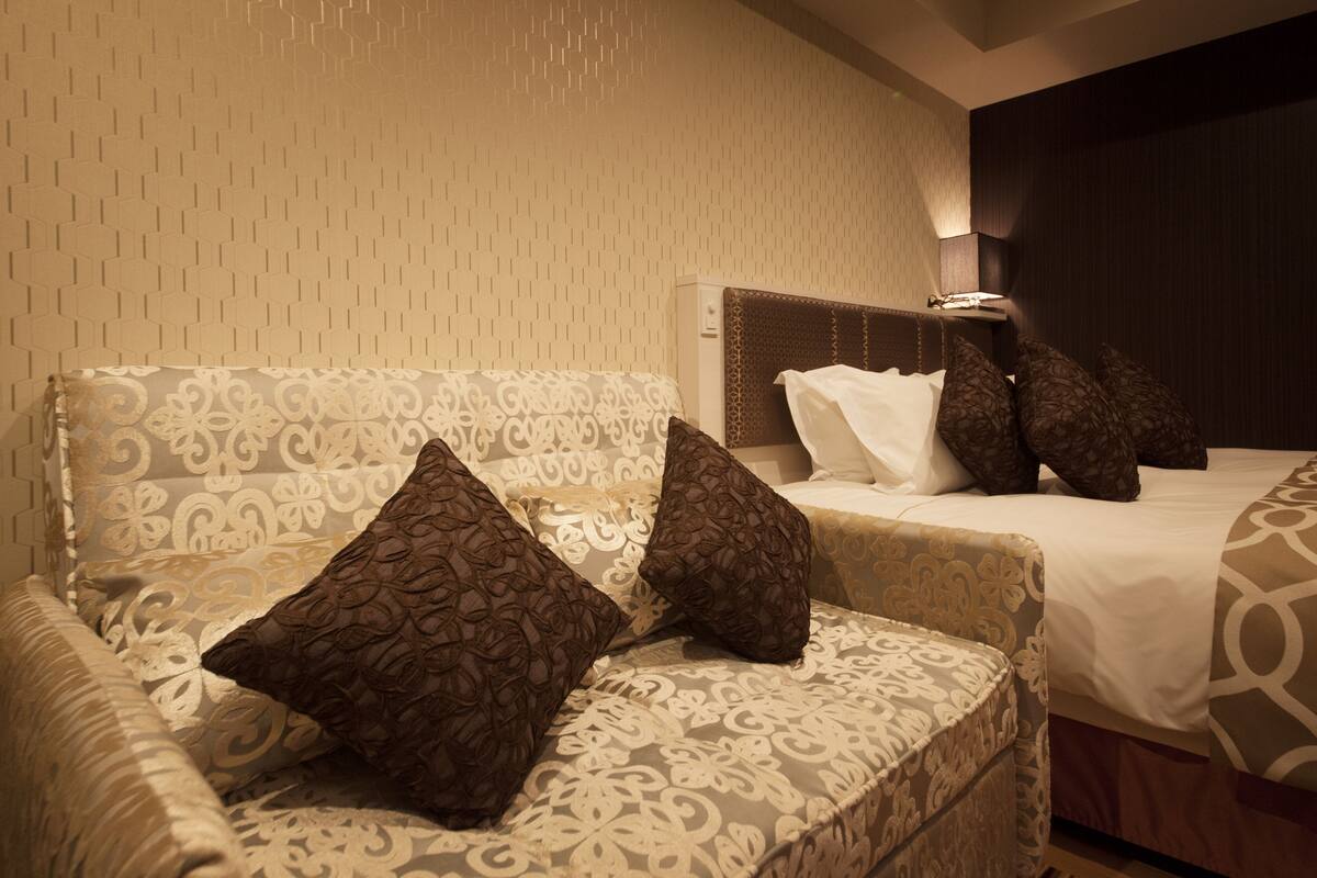 A hotel room with a patterned sofa and a bed with a headboard.