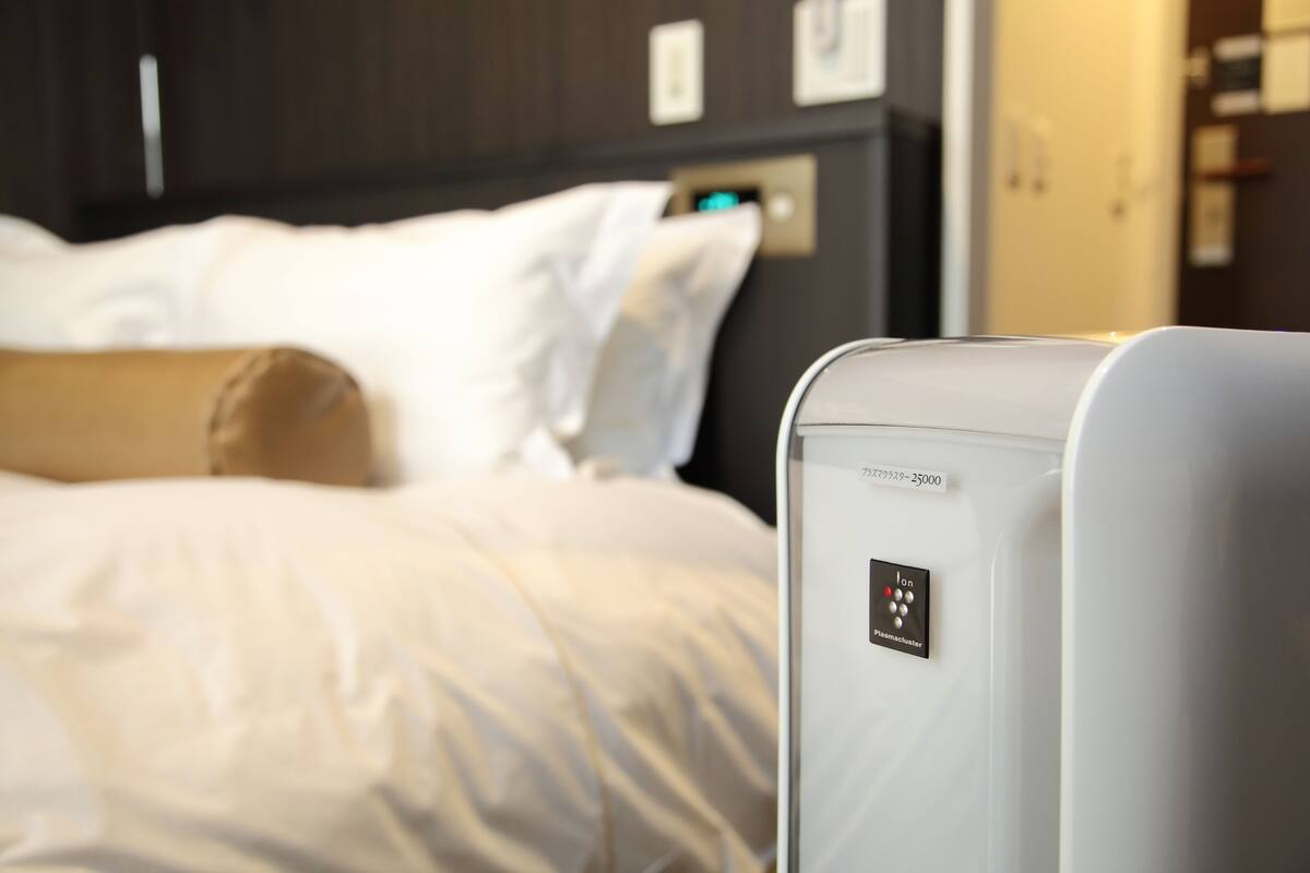 A hotel room with a bed, a control panel, and a wall-mounted device.