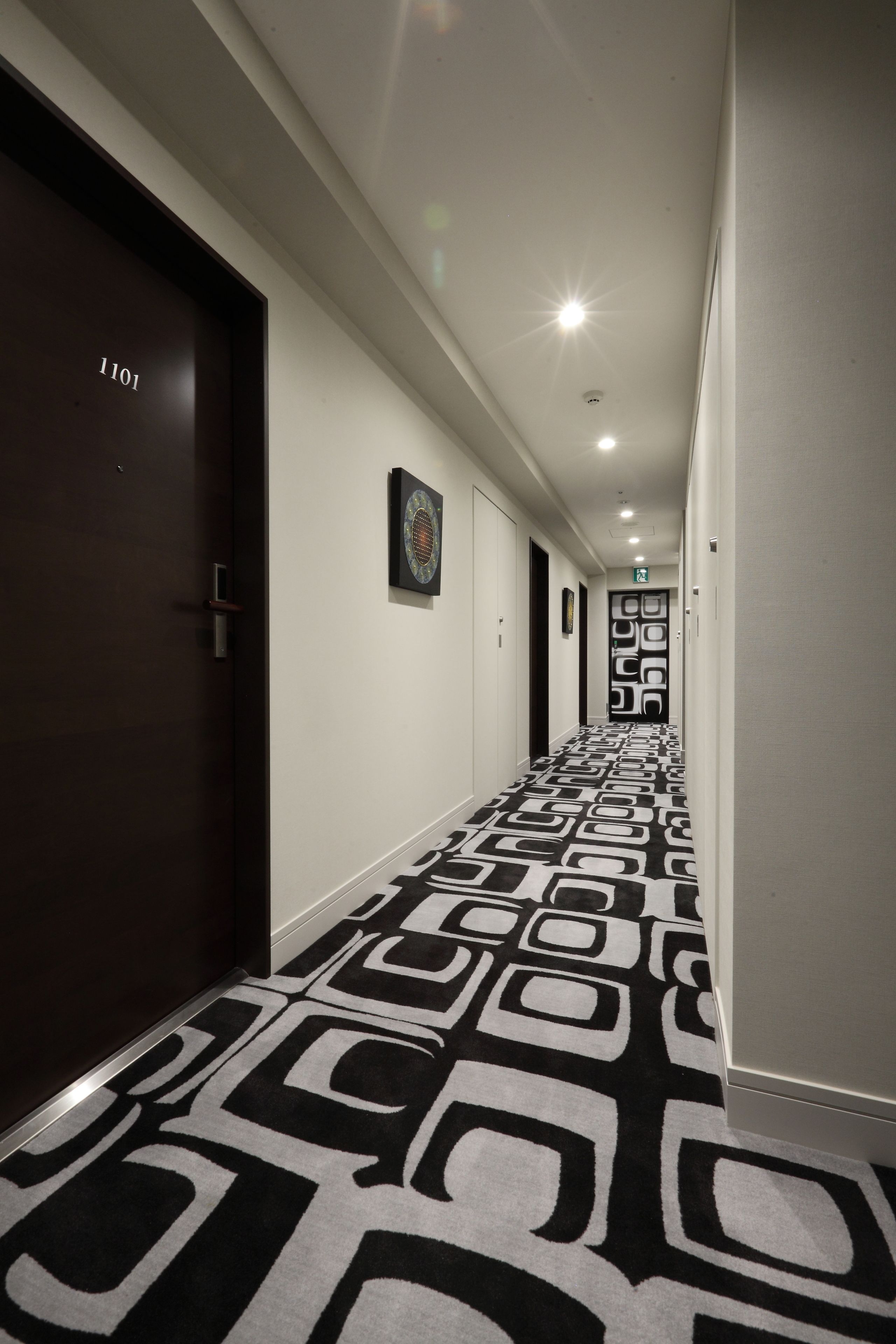 A hallway with patterned carpet, dark doors, and a framed picture on the wall.