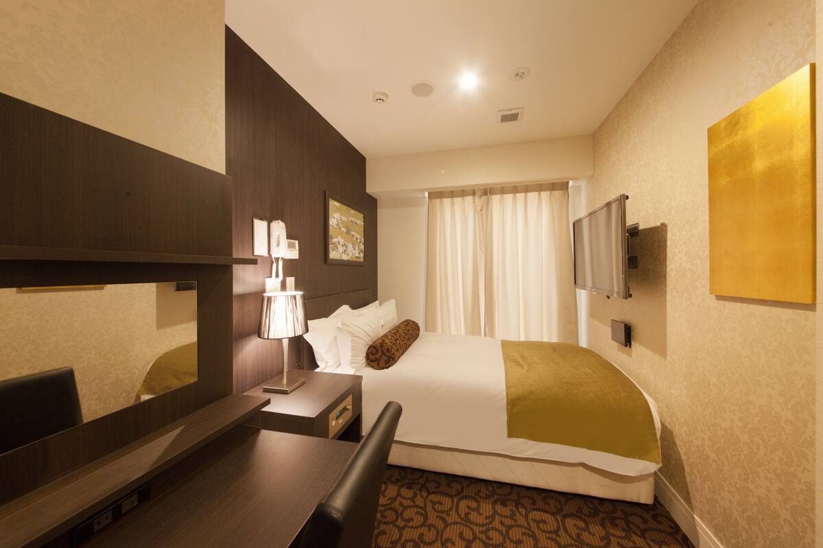 A hotel room with a bed, a desk, a chair, a TV, and a window with curtains.