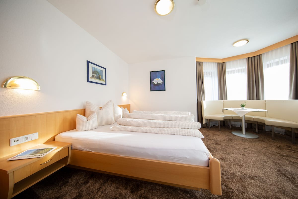 Ein Hotelzimmer mit Bett, Nachttisch, Lampe, Wandbild, Sofa und einem kleinen Tisch mit Pflanze.