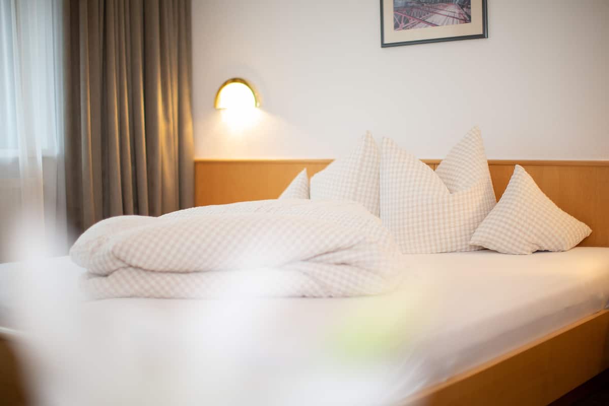 Ein ordentlich bezogenes Bett mit kariertem Überwurf und Kissen, ein Kopfteil, eine Wandleuchte und ein gerahmtes Bild an der Wand.