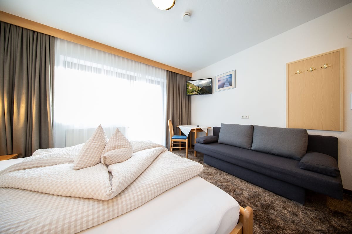 Ein Hotelzimmer mit Bett, einer Couch, einem an der Wand befestigten Fernseher und einem Fenster mit Vorhängen.