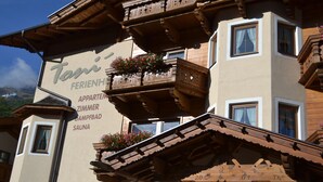 Un bâtiment traditionnel en bois, doté de balcons et d’une enseigne indiquant les équipements disponibles, tels que des appartements, des chambres, un spa et un sauna.