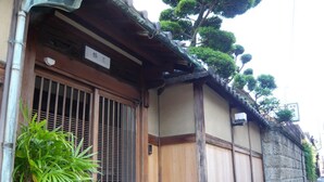 Un edificio japonés tradicional con puertas correderas de madera, un pequeño alero y un muro de piedra.