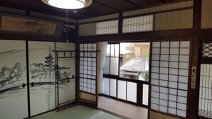 Una habitación tradicional japonesa con suelo de tatami, puertas correderas decoradas y vista a una zona residencial.
