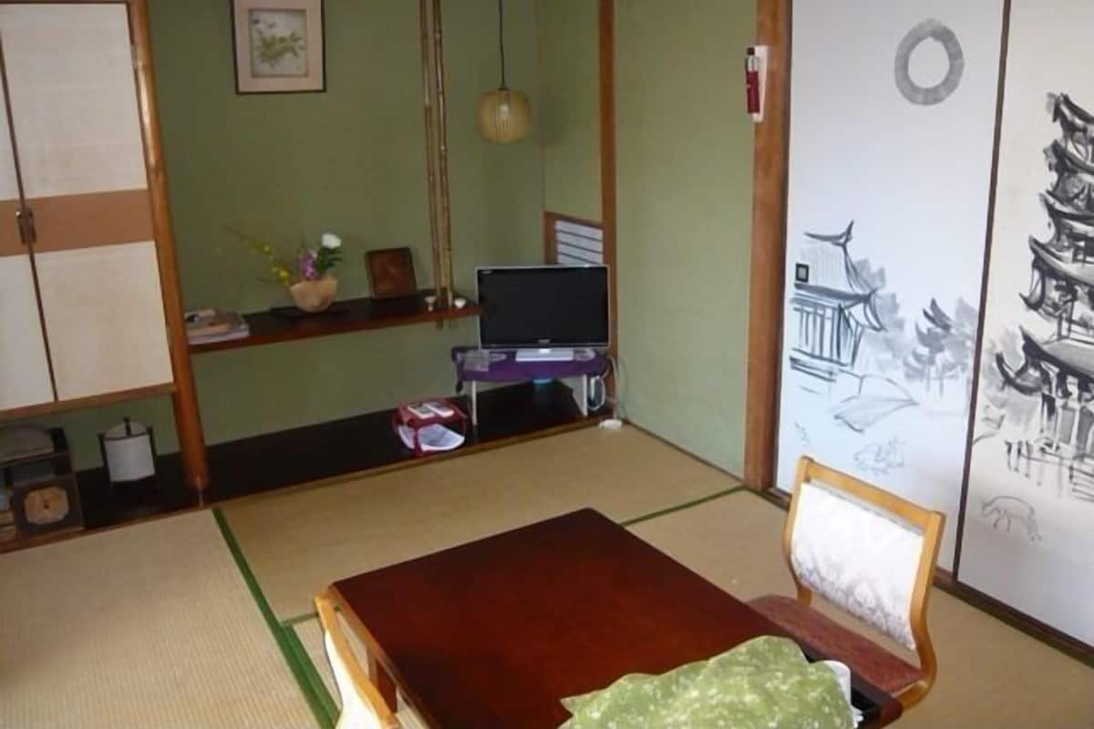 Una habitación japonesa tradicional con suelo de tatami, una mesa de madera baja, un televisor y un shoji con motivos decorativos.
