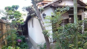Un sendero estrecho que lleva a un edificio blanco con techo inclinado, rodeado de abundante vegetación y un muro de piedra.